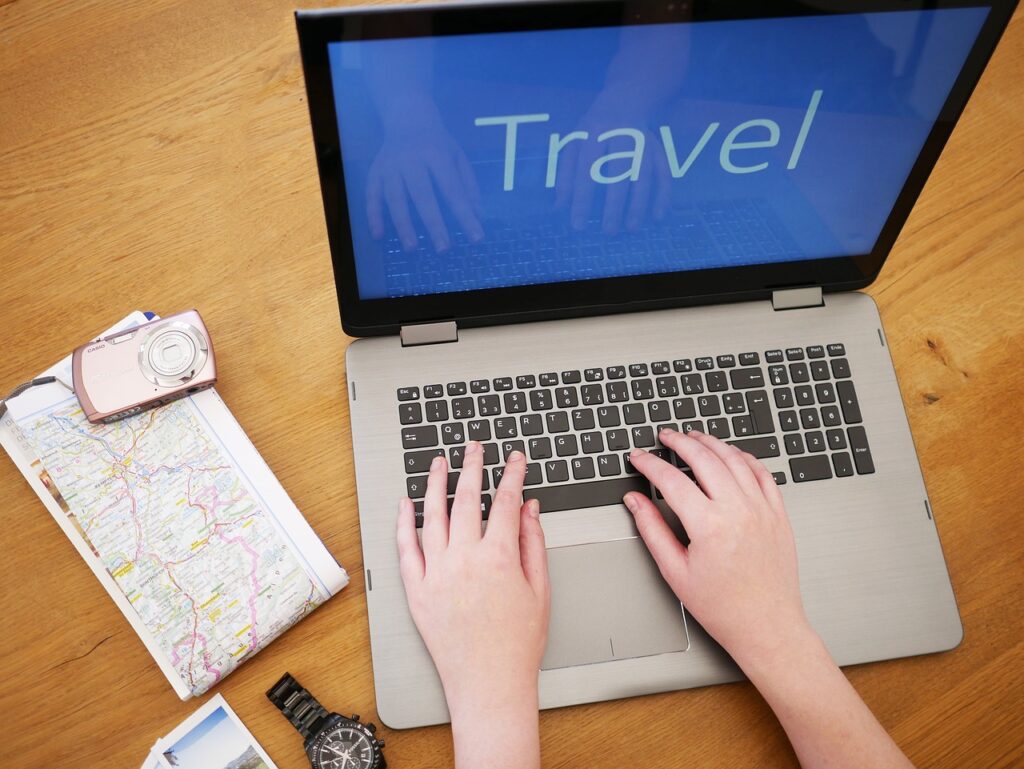 Ein Laptop steht auf aufgeklappt auf einem Tisch. Darauf steht das Wort Travel, welches auch im Beitrag OTA's Online Travel Agency vorkommt.